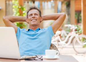A man is relaxing and smiling with his laptop and coffee
