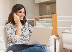 A woman is on the phone smiling with her laptop on her lap