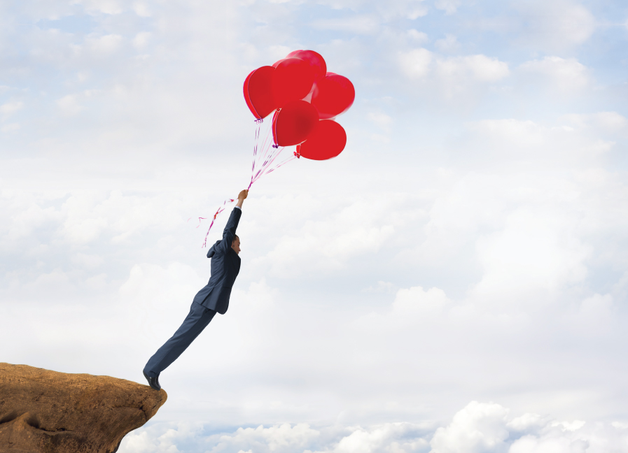 A business man holding red balloons on the edge of the rock cliff